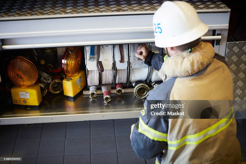 Rear view of firefighter arranging fire hose in engine at fire station