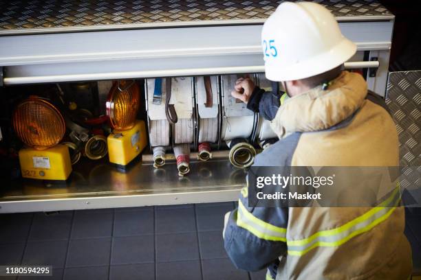 rear view of firefighter arranging fire hose in engine at fire station - fire truck stock pictures, royalty-free photos & images