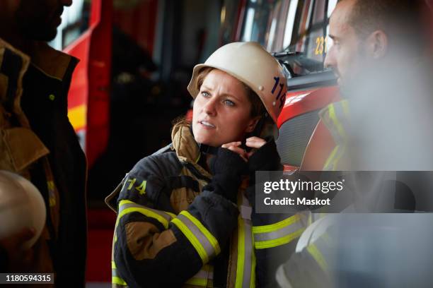 female firefighter wearing helmet while talking with other coworkers in fire station - feuerwehr stock-fotos und bilder