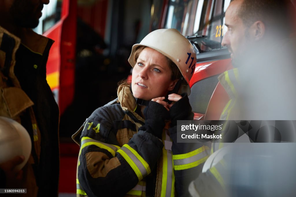 Female firefighter wearing helmet while talking with other coworkers in fire station