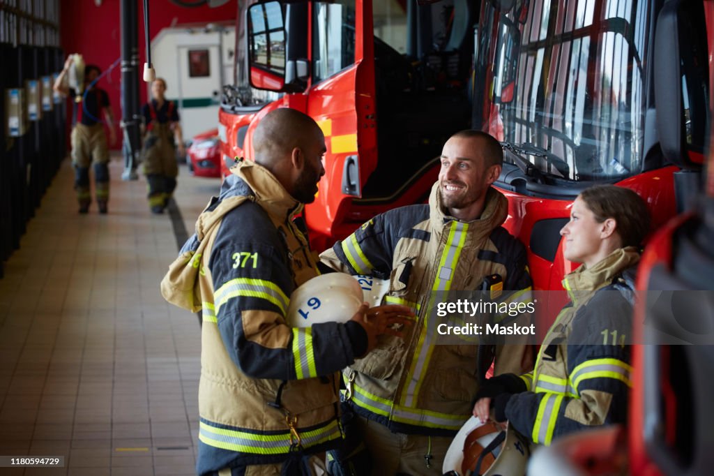 Firefighters in uniform talking while standing at fire station