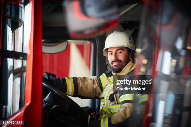 portrait of confident male firefighter sitting in fire engine at fire station - pompier photos et images de collection