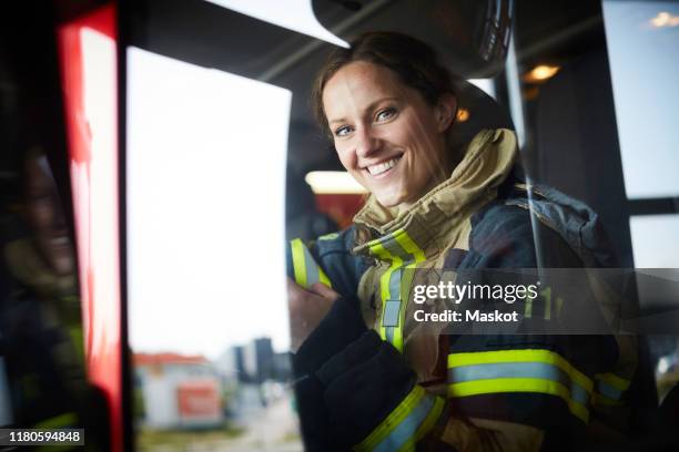 portrait of smiling female firefighter sitting in fire engine - firefighter stock pictures, royalty-free photos & images