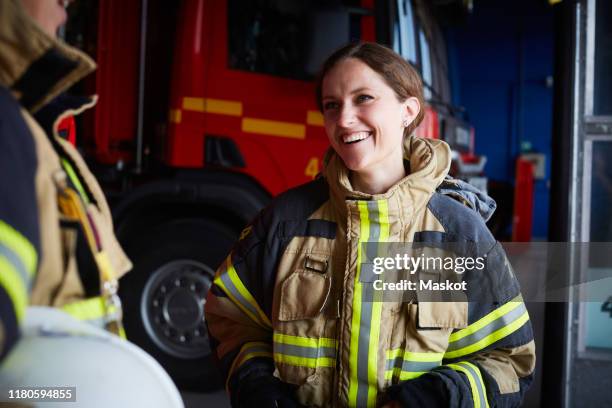 smiling female firefighter looking at coworker while communicating in fire station - firefighter foto e immagini stock