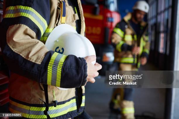 midsection of female firefighter with protective helmet standing at fire station - firefighters helmet stock pictures, royalty-free photos & images