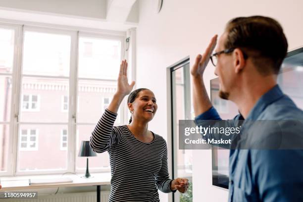 happy businesswoman giving high-five to male colleague in office - choque de manos en el aire fotografías e imágenes de stock