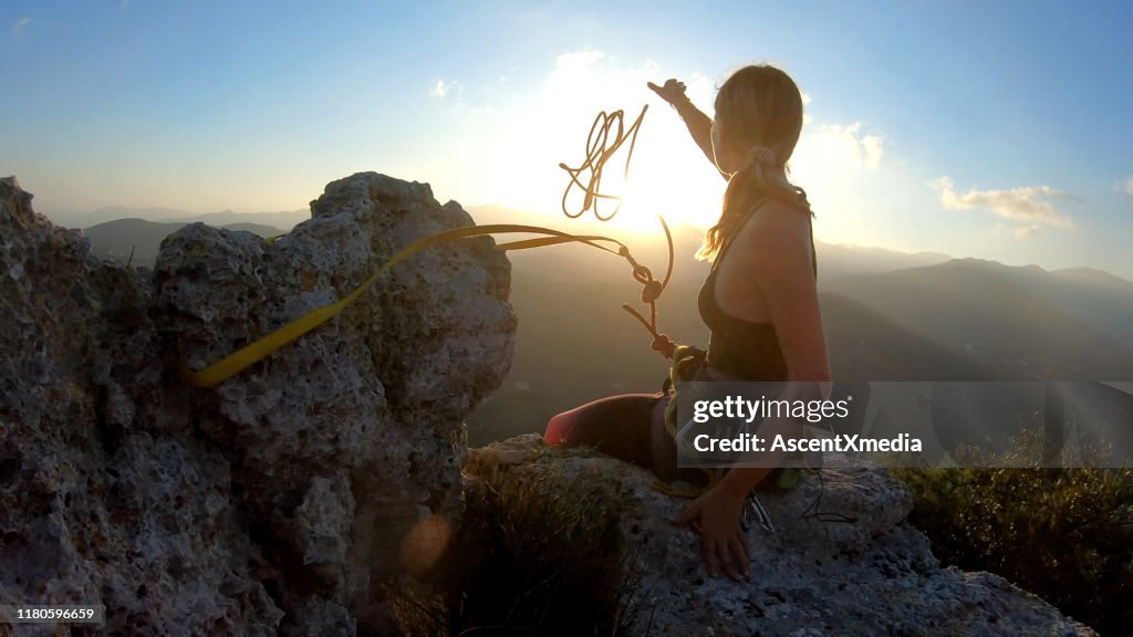 Young woman prepares to descend, throws rope from summit