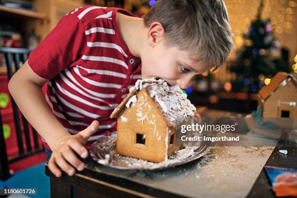 kleiner junge beginnt, das lebkuchenhaus zu essen - gingerbread house stock-fotos und bilder