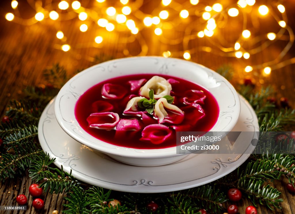 Christmas beetroot soup, red borscht with small dumplings with mushroom filling in a ceramic white plate on a wooden table