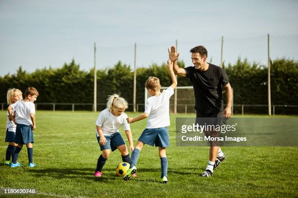 fußballtrainer high-fiving mit jungen während des trainings - sportbegriff stock-fotos und bilder