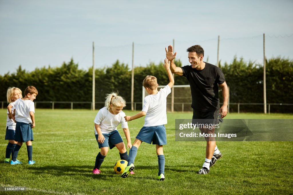 Soccer coach high-fiving with boy during practice