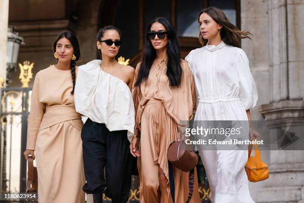 Bettina Looney wears earrings, a beige dress, a brown bag ; Anna Rosa Vitiello wears sunglasses, a gathered flowing asymmetric one-shoulder white...