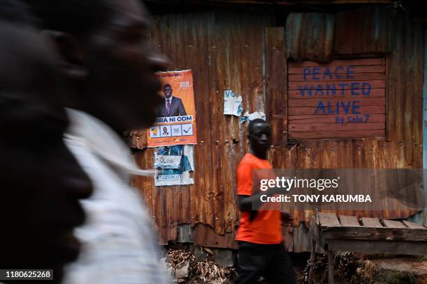 People walk past graffiti by a local artist on a residence, calling for peace during elections, on their way to nearby a polling station in Nairobi's...