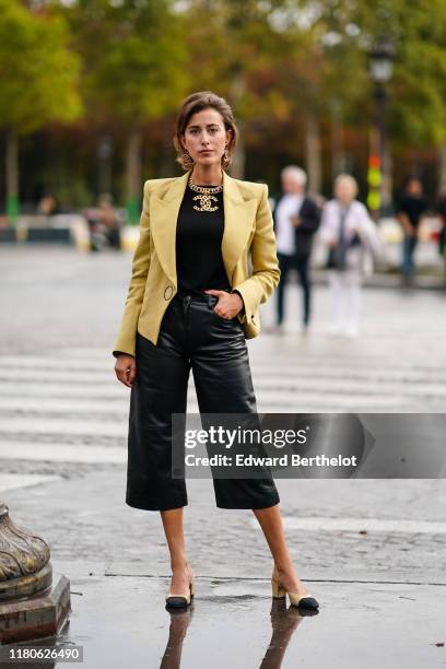 Sylvia Haghjoo wears Chanel earrings, a Chanel necklace, a yellow jacket, a black top, black leather wide-legs crop pants, Chanel slingback pumps,...