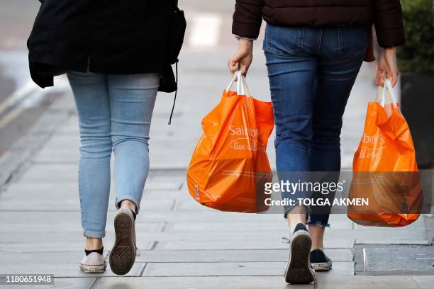 Shoppers carry their purchases in orange plastic Sainsbury's supermarket store shopping bags as they walk in London on November 7, 2019. -...