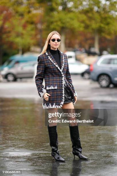 Pernille Teisbaek wears sunglasses, earrings, a black turtleneck, black leather shorts, a white trimmed brown and grey plaid jacket, black crocodile...