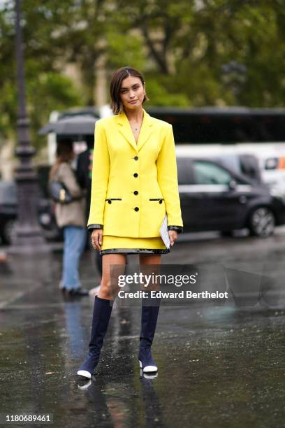 Sarah Ellen wears a yellow jacket, a necklace, a yellow and black skirt, navy blue high boots, outside Chanel, during Paris Fashion Week - Womenswear...