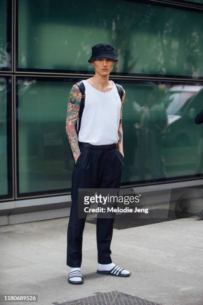 Model Wei Qi wears a black bucket hat, white sleeveless top, blue pants, and white socks with slide sandals after the Emporio Armani show during the...