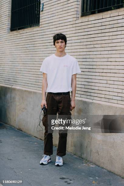 Model Eliot Moles le Bailly wears a white Qasimi "We Are So Different Now" t-shirt, brown pants, and white sneakers after the Neil Barrett show...