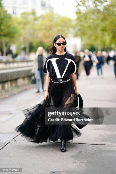 Yuwei Zhangzou wears sunglasses, a black Valentino t-shirt with printed large "V" logo, a black lace mesh skirt, a white studded bag from Valentino,...