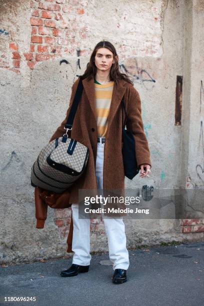 Model Dylan Christensen wears a long brown felt jacket, white jeans, black boots, and carries a large Gucci duffle bag after the Marni show during...