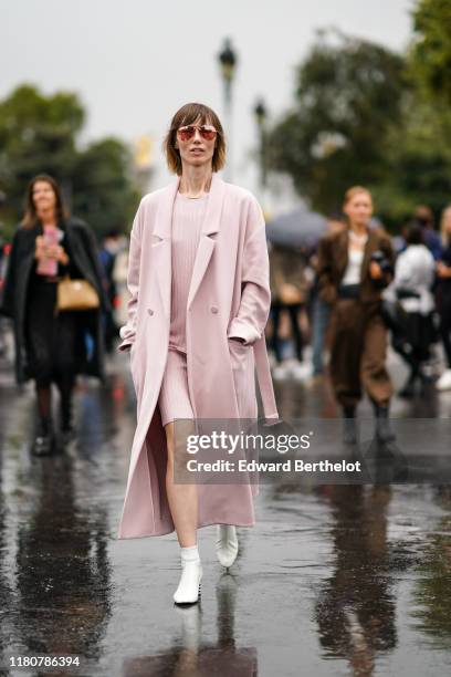 Anya Ziourova wears sunglasses, a pink long coat, a pink top, a pink skirt, white shoes, outside Chanel, during Paris Fashion Week - Womenswear...