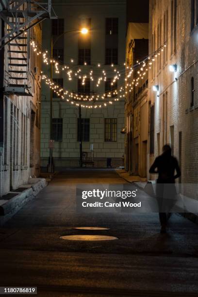 a deserted alley at night with a silhouetted figure - dark alley stock pictures, royalty-free photos & images