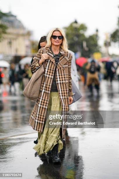 Guest wears sunglasses, a brown checked pattern long coat, a khaki green skirt, a large wool bag, a black shirt, black shoes, outside Chanel, during...