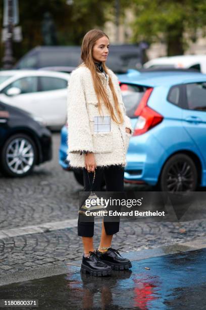 Guest wears a white wool jacket and golden and black striped pyramid Chanel bag, black cropped pants, black leather shoes, outside Chanel, during...