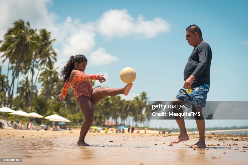 Father playing soccer with his daughter on the beach