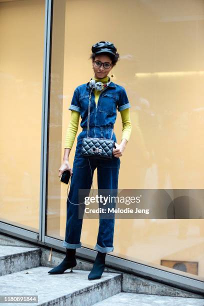 Model Lineisy Montero wears a black leather newsboy cap, Mickey Mouse Beats headphones, a a short-sleeve denim jumpsuit over a yellow top, black...