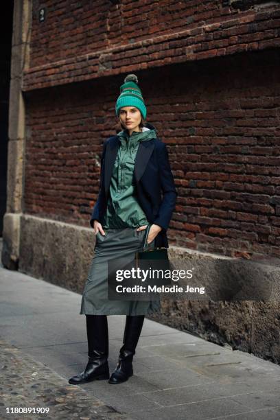 Model Giedre Dukauskaite wears a green Patagonia pom hat, blue blazer, green Patagonia zip jacket, green skirt, green Celine bag, and black boots...