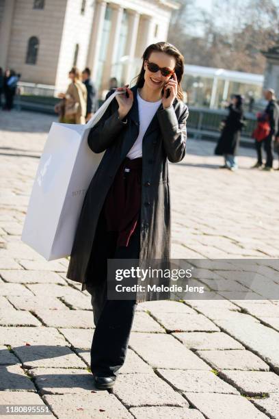 Model talks on the phone, wears a black leather trenchcoat, and carries a large Bottega Veneta shopping bag after the Bottega Veneta show on Day 3...