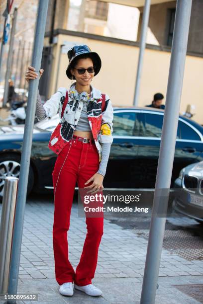 Model Lineisy Montero wears a black leather bucket hat, Mickey Mouse Beats headphones, a Mickey Mouse white denim jacket, red jeans, and white...