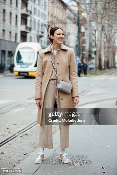 Model Ania Chiz wears a camel peacoat, Prada cross-body bag, tan pants, and light pink sneakers after Dolce & Gabbana on Day 5 Milan Fashion Week...