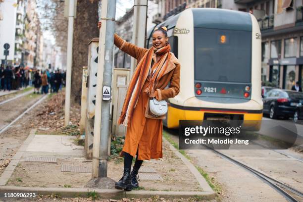 Model Aaliyah Hydes wears a brown shearling jacket, orange scarf, orange dress, white Chloe bag, and black boots Model after Dolce & Gabbana on Day 5...