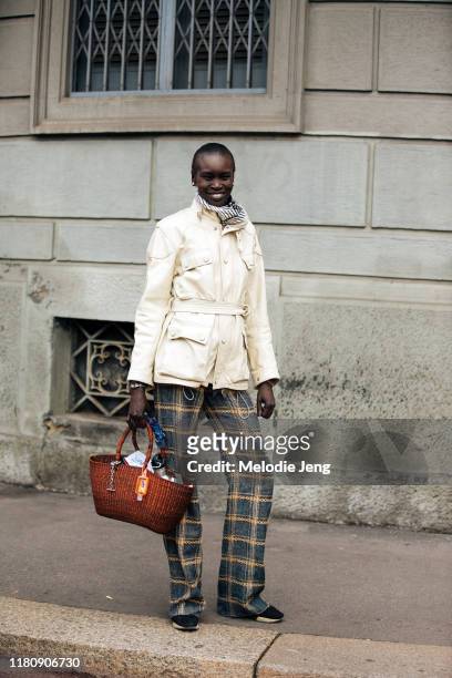 Model Alek Wek wears a white belted leather jacket, printed pants, and a woven brown bag after the Salvatore Ferragamo show on Day 4 Milan Fashion...