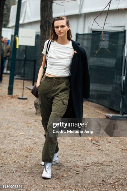 Model Natalie Ogg wears a white t-shirt, black jacket, green pants, and white J.W. Anderson x Converse sneakers after the Roberto Cavalli show on Day...