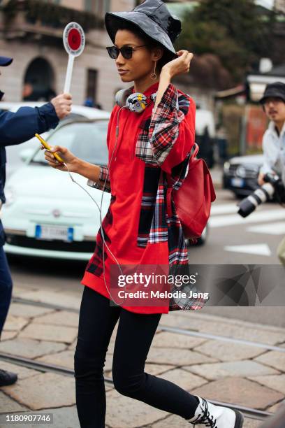 Model Lineisy Montero wears a black bucket hat, Mickey Mouse Beats headphones, red plaid shirt, and black skinny jeans after the Roberto Cavalli show...