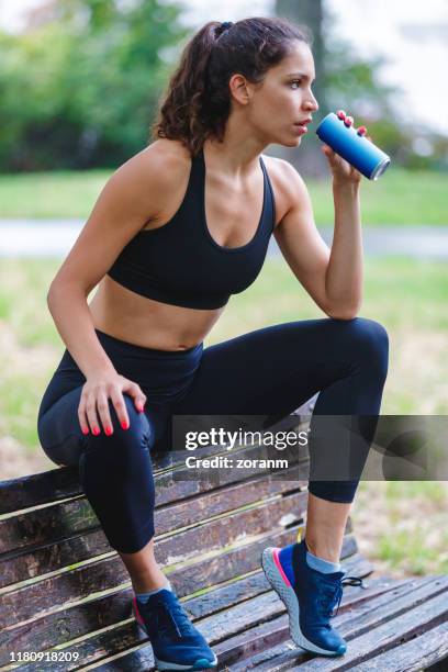 jonge vrouwelijke jogger houden van een drankje op de bank van het park - blank can stockfoto's en -beelden