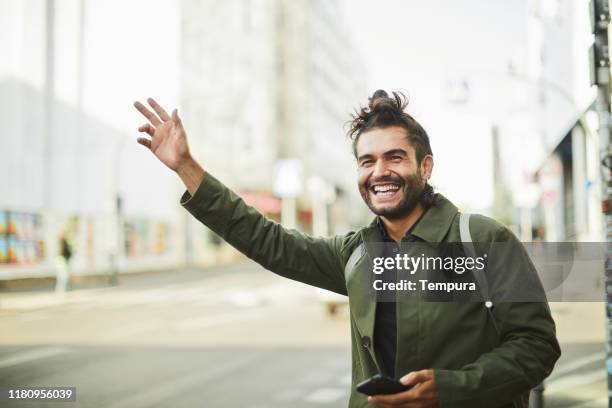 young man in the streets of berlin hailing a taxi. - carsharing stock pictures, royalty-free photos & images