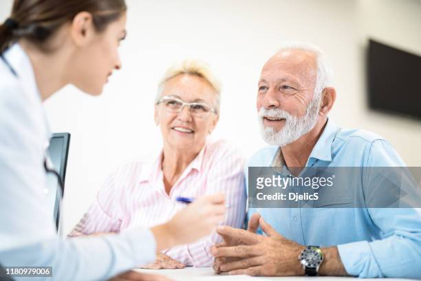 young female doctor giving advice to happy senior couple. - couple doctor stock pictures, royalty-free photos & images