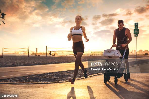 amazing modern and young family running on the beach at sunset - three wheeled pushchair stock pictures, royalty-free photos & images