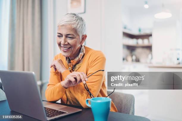 smiling senior woman using laptop at home - blogger woman stock pictures, royalty-free photos & images