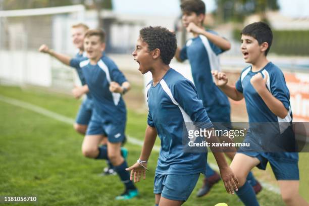 team van zelfverzekerde jonge mannelijke voetballers die op het veld rennen - voetbalcompetitie sportevenement stockfoto's en -beelden