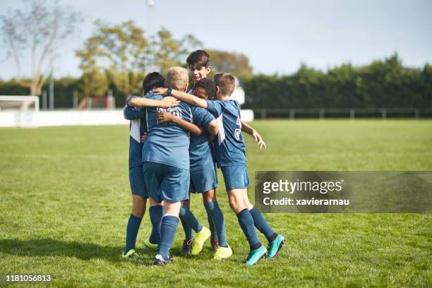 young male footballers in huddled embrace on field - football huddle stock pictures, royalty-free photos & images