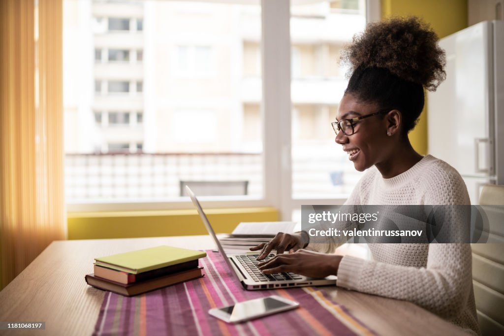 Afro Woman sitting at home using laptop and studying