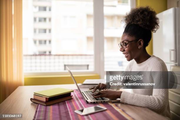 afro woman sitting at home using laptop and studying - communication wireless technology students stock pictures, royalty-free photos & images
