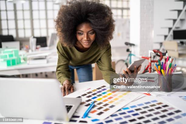 afrikaanse modeontwerper werken in studio en het gebruik van laptop en smart phone - grafisch ontwerpbureau stockfoto's en -beelden