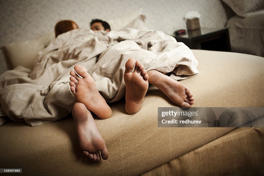 Couple in bed with feet hanging out the covers